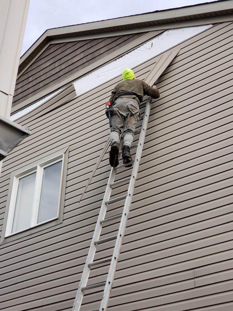 Man on ladder repairing some damaged siding on house
